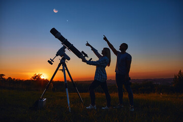 Couple stargazing together with a astronomical telescope.
