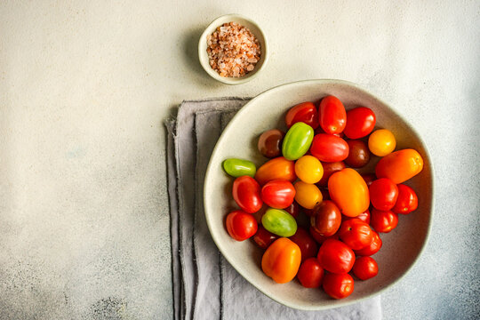 Overhead view of a bowl of multi coloured cherry tomatoes on a folded napkin with a bowl of salt