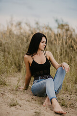 brunette girl with long hair in a black corset and blue jeans in a field