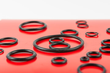 Black hydraulic and pneumatic o-rings in different sizes on a red and white background. Rubber rings. Sealing gaskets for hydraulic connections. Rubber sealing rings for plumbing. blurred background