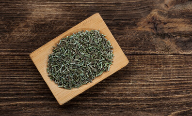 Dried rosemary on dark wooden background.
A wooden plate filled with dried chopped rosmary, top view.

