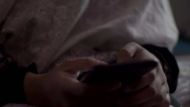 An extreme close up shot of the hands of a young Muslim teenage girl wearing a Hijab, her fingers navigating through different applications on her mobile phone