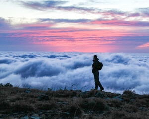 silhueta de homem com mochila nas costas caminhando na montanha ao amanhecer com mar de nuvens ao...