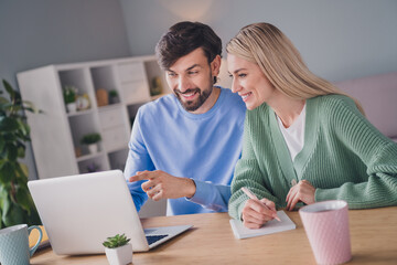 Portrait of two attractive cheerful people using laptop choosing order goods web service at home indoors