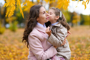 Fototapeta premium Mother and daughter portrait in an autumn park. Happy people pose against the background of beautiful yellow trees. They hug and are happy together.