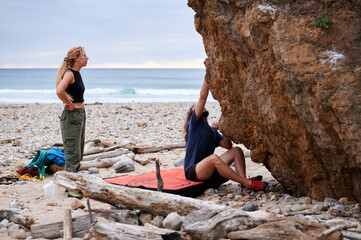 Male climber sitting on coast of sea during ascending practice on coast of waving blue sea with partner