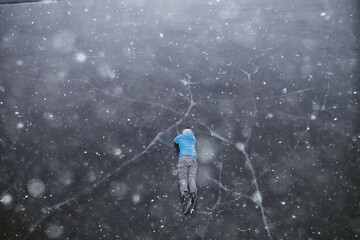 a man in ice skates lies on the transparent ice of the lake, view from above, aerial photography