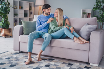 Full length photo of positive cheerful spouses sit divan man cuddle hug embrace his lady enjoy room...