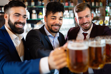 Cheerful old friends having fun and drinking beer at bar counter in pub.