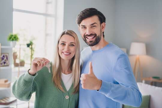 Portrait of two handsome beautiful cheerful people partners holding in hands key showing thumbup at home indoors