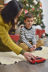 Happy kid playing with car toy on Christmas Eve. Mom play with son with new toy for New Year