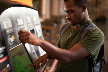 Smiling African man using ATM machine. Happy young  man withdrawing money from credit card at ATM
