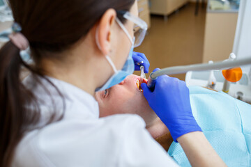 Fototapeta premium Woman dentist while treating a patient. The doctor makes dental treatment on the teeth of a person in the dentist's chair. Selective focus.