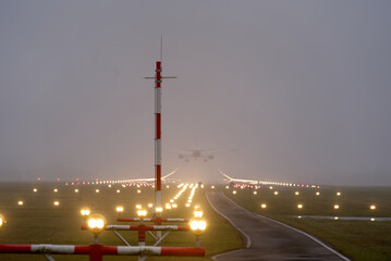 Landing airplane with spotlights at runway of the airport on a foggy winter day. Photo taken...