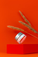 Balanced cream glass jar mockup on geometrical podium orange background dry reeds pampas grass. Natural eco-friendly anti aging skin cosmetic moisturizer SPA skincare product Wellness facial hydration