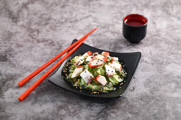 Crab and cucumber salad served on dark dish. Sunomono, slim cucumber slices. Studio shoot.