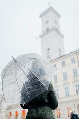 Woman walking in Lviv city center by town hall holding umbrella under snow. Tourist enjoys architecture in winter