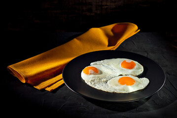 Scrambled eggs in a black plate. Fried eggs on an old concrete table. Yellow tablecloth near the plate.