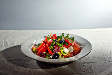 Salad with tomatoes, peppers, olives, cheese and cabbage. Fresh salad in a white plate on a light background. Copy space and free space for text near food.