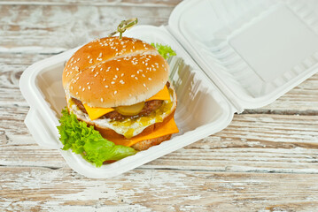 Cheeseburger in a white plate on an old shabby table. Burger and french fries close up. Food in an ecological container made from processed corn. Environmentally friendly dishes.