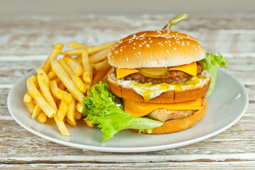 Cheeseburger in a white plate on an old shabby table. Burger and french fries close up.