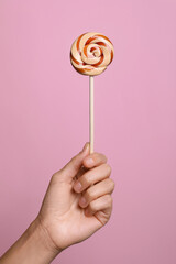 Woman holding bright tasty lollipop on pink background, closeup
