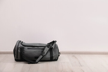 Grey sports bag on floor near white wall, space for text