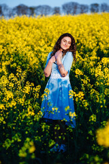 Naklejka na ściany i meble Portrait of a happy female student holding books and looking at camera outdoors. Young, beautiful girl holding a Bible in her hands, against the background of yellow flowers in the field.