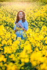 Naklejka na ściany i meble Happy girl hugs the bible in the sunlight on a background of yellow flowers. Girl with a book outdoors. Concept for faith, spirituality and religion. Peace, hope
