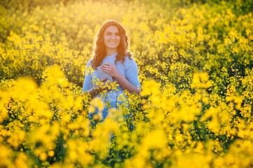 Naklejka na ściany i meble Happy girl hugs the bible in the sunlight on a background of yellow flowers. Girl with a book outdoors. Concept for faith, spirituality and religion. Peace, hope