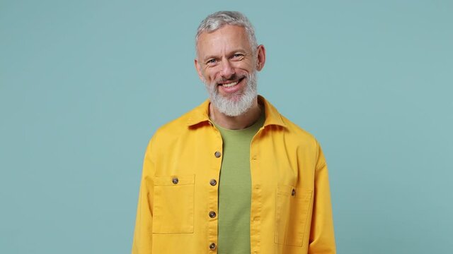 Happy charismatic ecstatic elderly gray-haired bearded man 50s wears yellow shirt look camera smiling isolated on plain pastel light blue background studio portrait. People emotions lifestyle concept