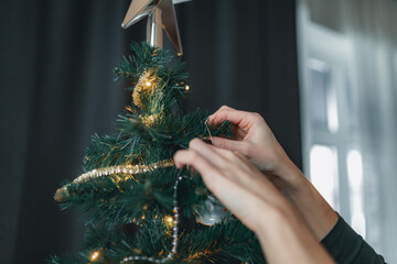 Girl decorates Christmas tree with bright glass balls, stars and a garland.