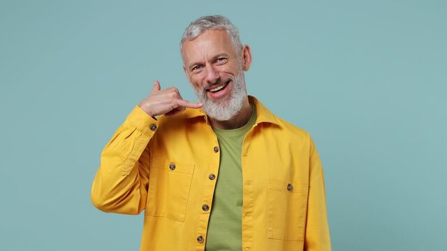 Happy fun elderly gray-haired bearded man 50s wears yellow shirt point finger camera on you doing phone gesture like says call me back isolated on plain pastel light blue background studio portrait
