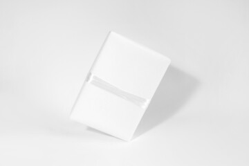 One gift box in white wrapping paper with white rope on white table. Isolated wrapped gift mock up with ribbon.