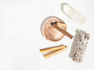 Items for spiritual cleansing - sage bundle, palo santo incense sticks and quartz crystal on white...