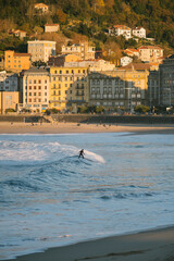 Female surfer reaching the shore on a small wave during sunset in San Sebastian beach