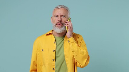 Perplexed angry sad elderly gray-haired bearded man 50s wears yellow shirt talking on mobile cell phone ask what bad news scream swear isolated on plain pastel light blue background studio portrait