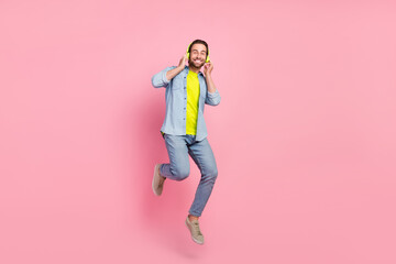 Full size photo of young cheerful guy have fun jump listen song playlist earphones isolated over pink color background