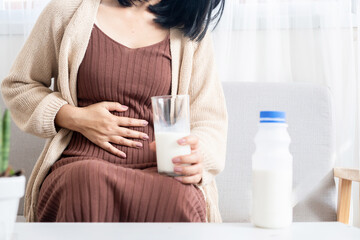 woman holding stomachache and a glass of cow milk having gas, heartburn, feeling discomfort because...