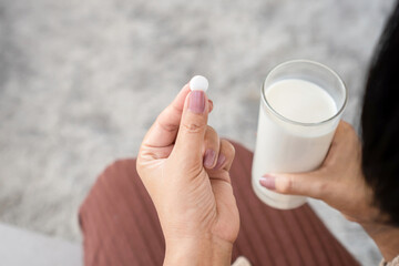 closeup woman taking medicine hand holding a glass of milk