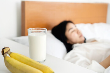 a glass of milk and bananas on the table with blur background of woman sleeping in bed, eating...