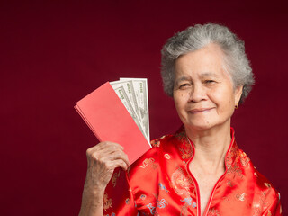 Senior woman wearing a traditional cheongsam qipao dress holding Angpao with US dollar banknote while standing over a red background