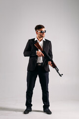A young guy in a black suit with a gun in his hands on a white background in the studio, he depicts a security guard, bodyguard or Agent
A young guy in a black suit with a gun in his hands on a white 
