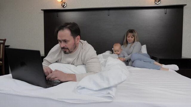Dad is a freelancer, works at the computer at home, mom plays with the child. Family with a child. Dad works at home at the computer, mom and baby with a child with a digital tablet.