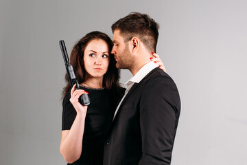 young couple, in black suits with pistols in their hands on a white background in the studio, they depict security guards, bodyguards or agents.