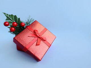 Red gift box on a blue background. A sprig of a Christmas tree, rowan. New Year's gift. Surprise. Christmas.