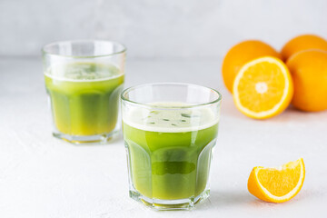 Matcha and orange juice drink in glasses on a light table.