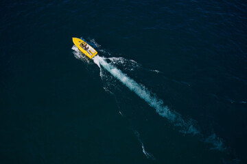 Boat performance fast movement on the water aerial view. High-speed luxury yellow boat with people moving on dark blue water.