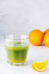 A cocktail of matcha and orange juice with ice in a glass on a light background.