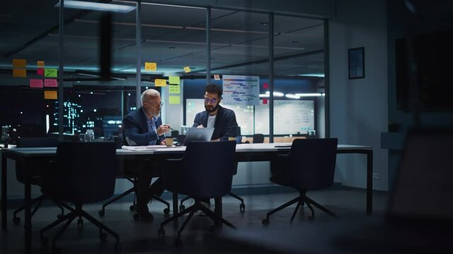 Businesspeople in Modern Office: Business Meeting of Two Managers. CEO and Marketing Director Talk, Discuss, Brainstorm Corporate Strategy, Implementing Marketing and Financial Plans. Evening Time.